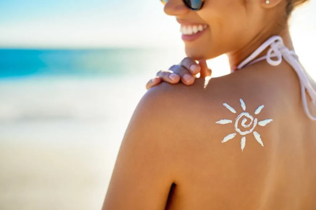 mujer frente a la playa, mostrando el símbolo de un sol en su hombro dibujado con protector solar